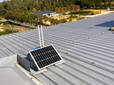 LoRa-Sensorknoten mit Solarpanel und Antennen, montiert auf einem Hallendach